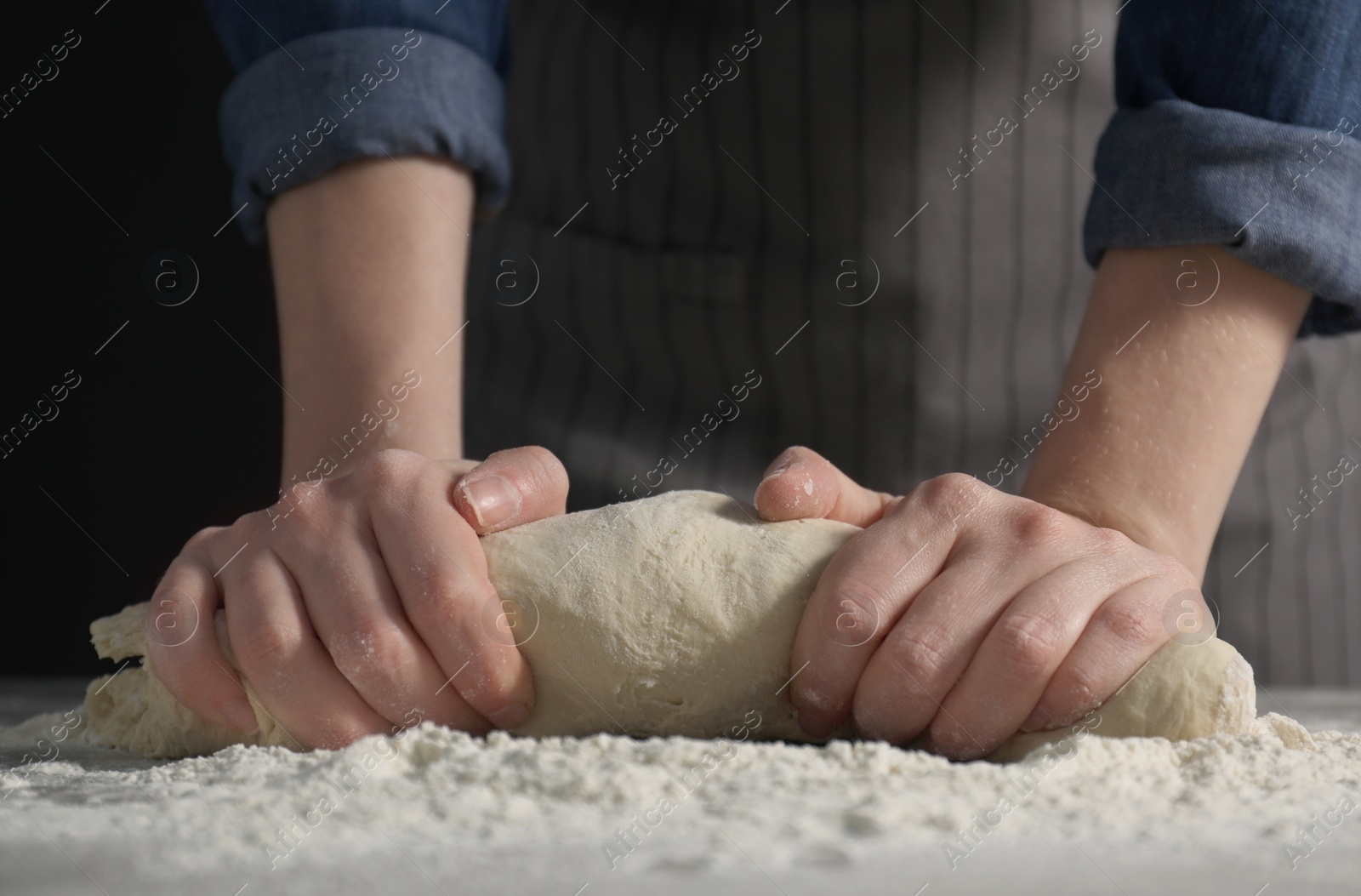 Photo of Making bread. Woman kneading dough at table on dark background, closeup