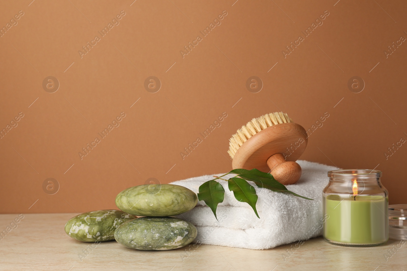 Photo of Composition with different spa products and burning candle on beige table against brown background. Space for text