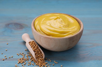 Photo of Sauce bowl with delicious mustard and seeds on light blue wooden table, closeup