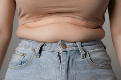 Overweight woman in tight jeans on grey background, closeup