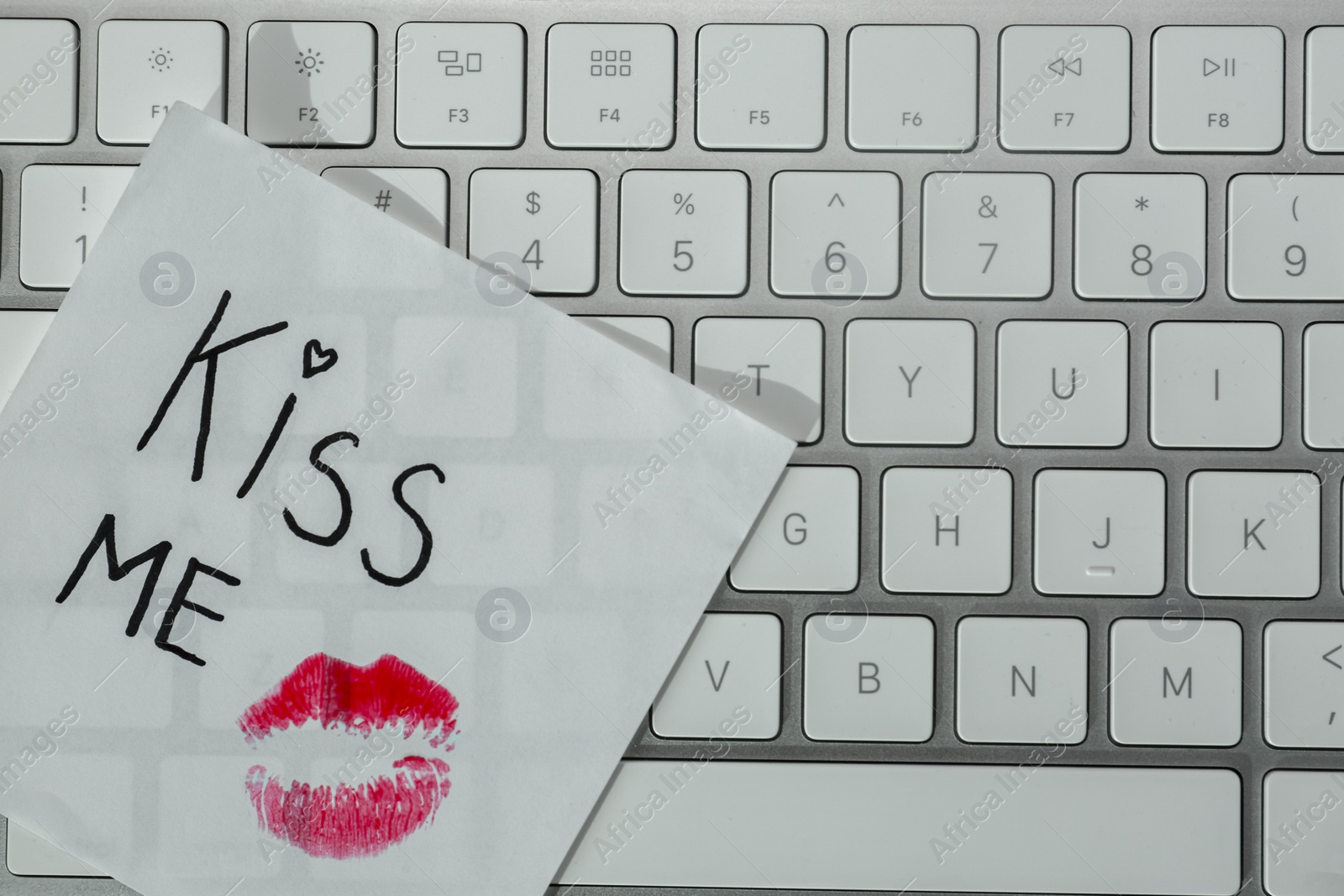 Photo of Sticky note with phrase Kiss Me and lipstick mark on keyboard, top view