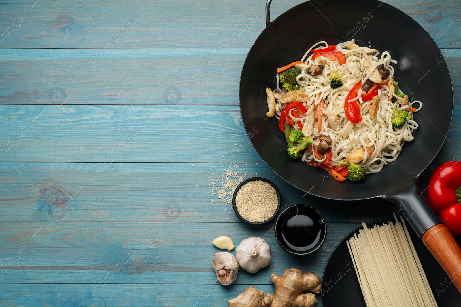 Photo of Stir fried noodles with mushrooms, chicken and vegetables in wok on light blue wooden table, flat lay. Space for text