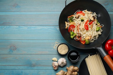 Photo of Stir fried noodles with mushrooms, chicken and vegetables in wok on light blue wooden table, flat lay. Space for text