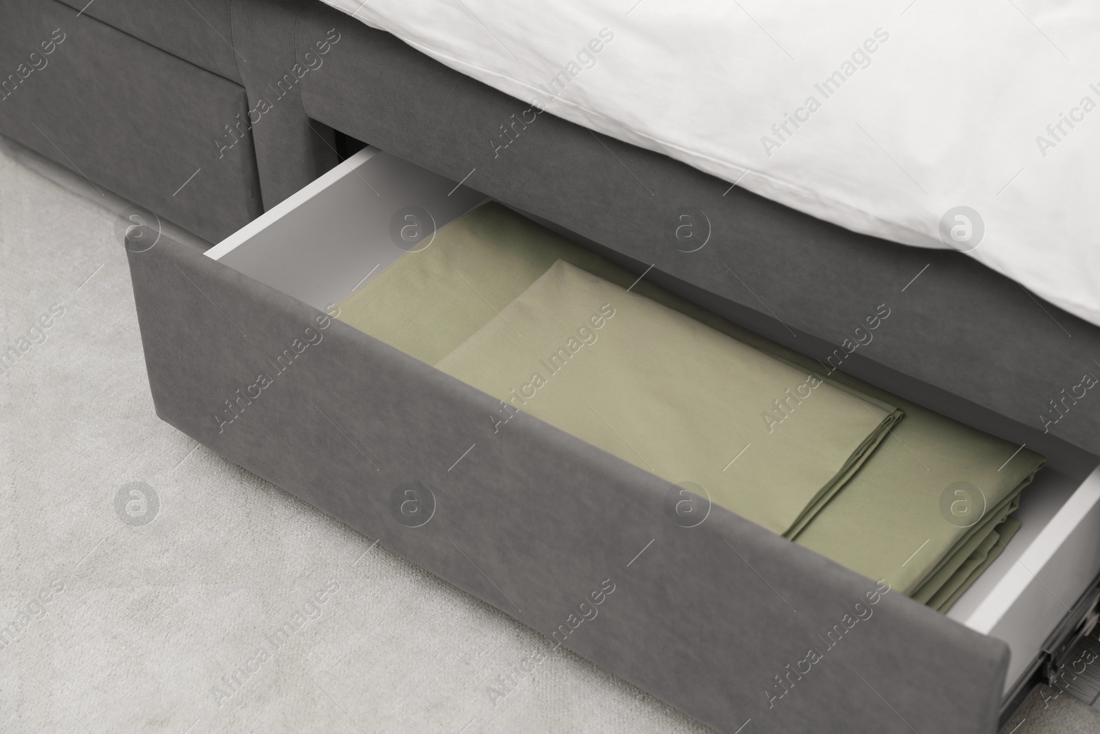 Photo of Storage drawer with bedding under modern bed in room, closeup