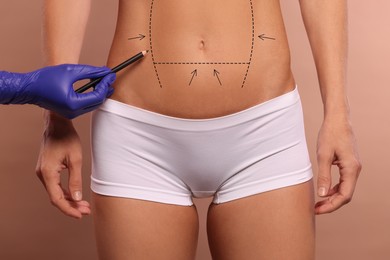 Image of Woman preparing for cosmetic surgery, light brown background. Doctor drawing markings on her abdomen, closeup