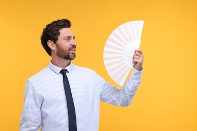 Happy man holding hand fan on orange background