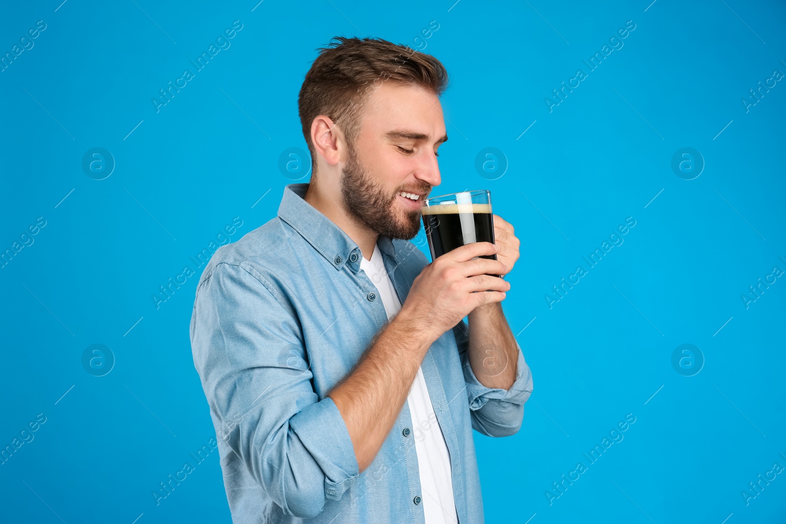 Photo of Handsome man with cold kvass on blue background. Traditional Russian summer drink