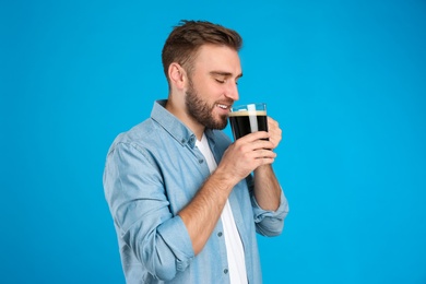 Photo of Handsome man with cold kvass on blue background. Traditional Russian summer drink