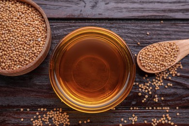 Photo of Bowl of natural oil and mustard seeds on wooden table, flat lay