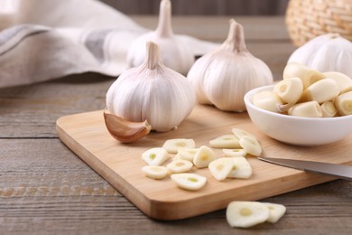 Photo of Aromatic cut garlic, cloves and bulbs on wooden table, closeup