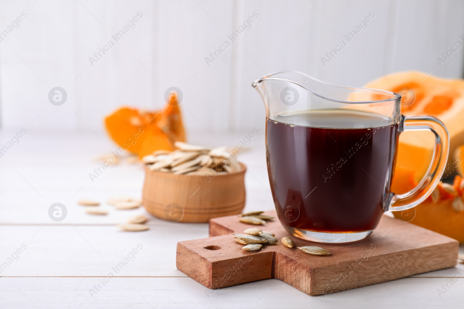 Photo of Fresh pumpkin seed oil in glass pitcher on white wooden table. Space for text