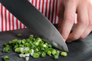 Woman cutting green spring onion on black wooden board, closeup