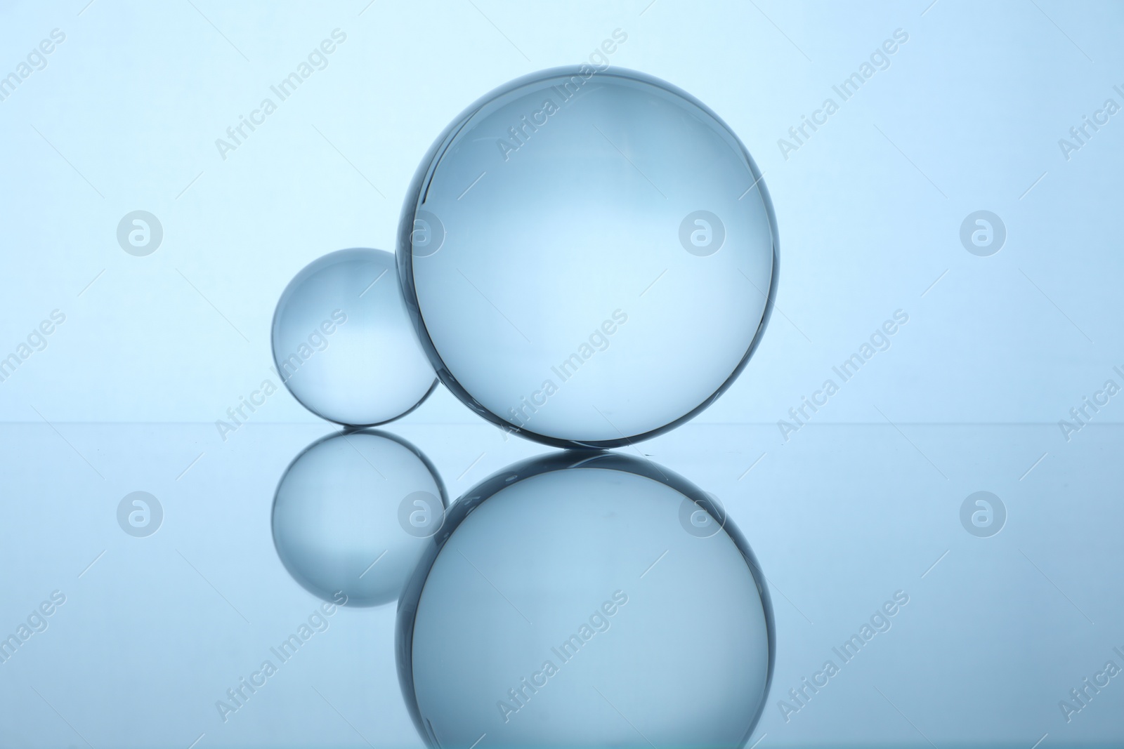 Photo of Transparent glass balls on mirror surface against light background