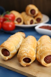 Photo of Delicious sausage rolls and ingredients on blue wooden table, closeup