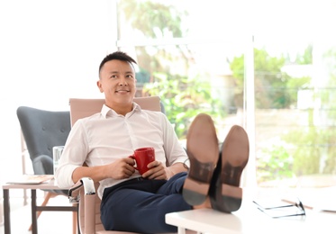 Happy young businessman with cup of coffee enjoying peaceful moment at workplace