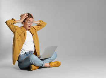 Photo of Emotional young woman with laptop on grey background. Space for text