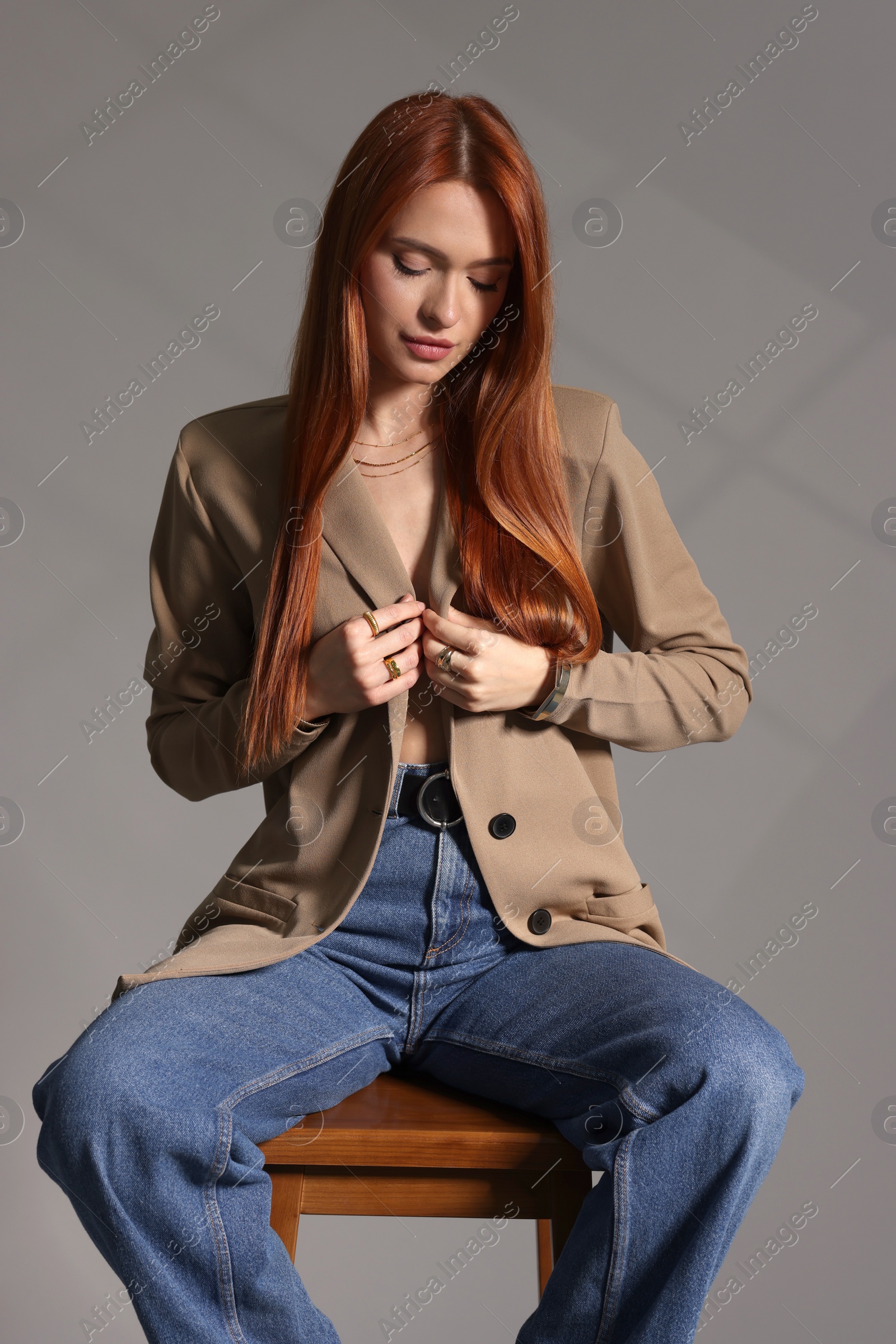 Photo of Beautiful young woman with elegant jewelry sitting on wooden stool against gray background