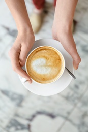 Photo of Young woman with cup of delicious coffee on blurred background