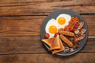 Plate of fried eggs, sausages, mushrooms, beans, bacon and toasted bread on wooden table, top view with space for text. Traditional English breakfast