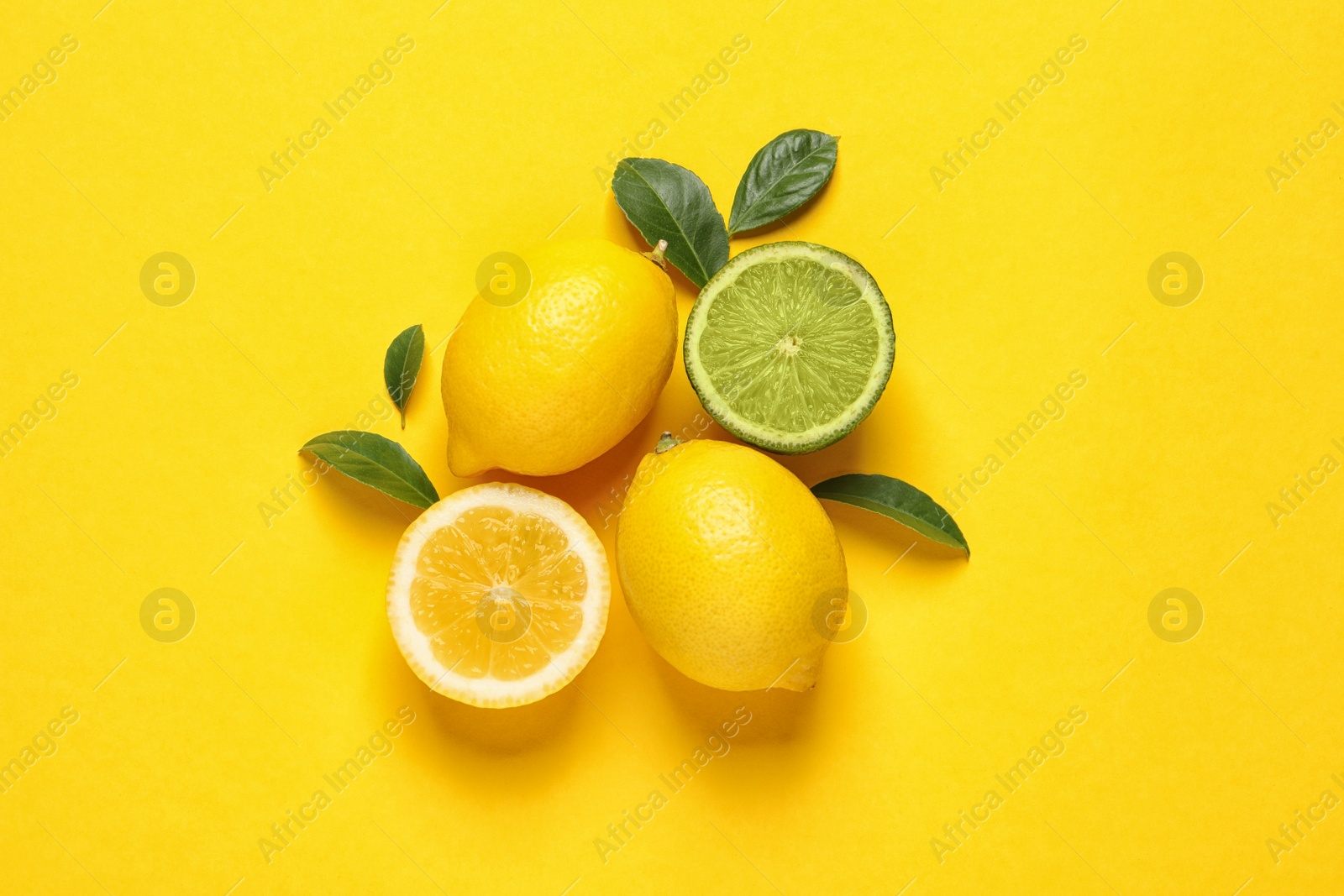 Photo of Fresh ripe lemons, lime and green leaves on yellow background, flat lay