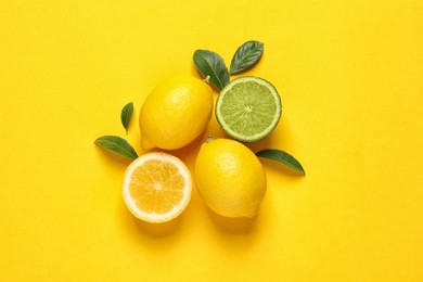 Photo of Fresh ripe lemons, lime and green leaves on yellow background, flat lay