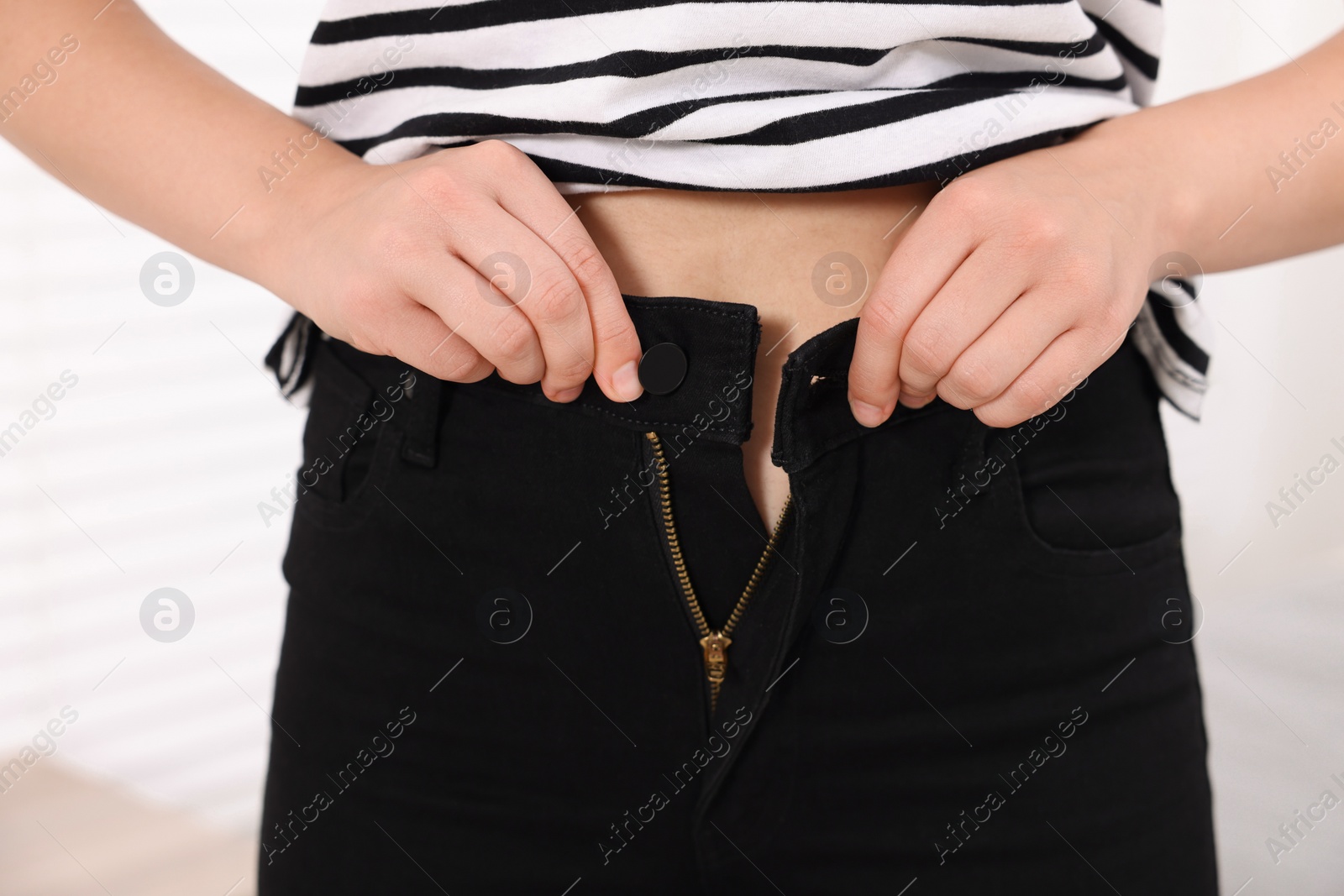 Photo of Woman trying to fit into her black jeans at home, closeup