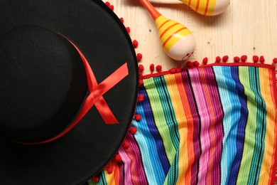 Photo of Mexican sombrero hat, maracas and colorful poncho on wooden background, flat lay