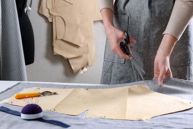 Tailor cutting fabric with scissors at table in atelier, closeup