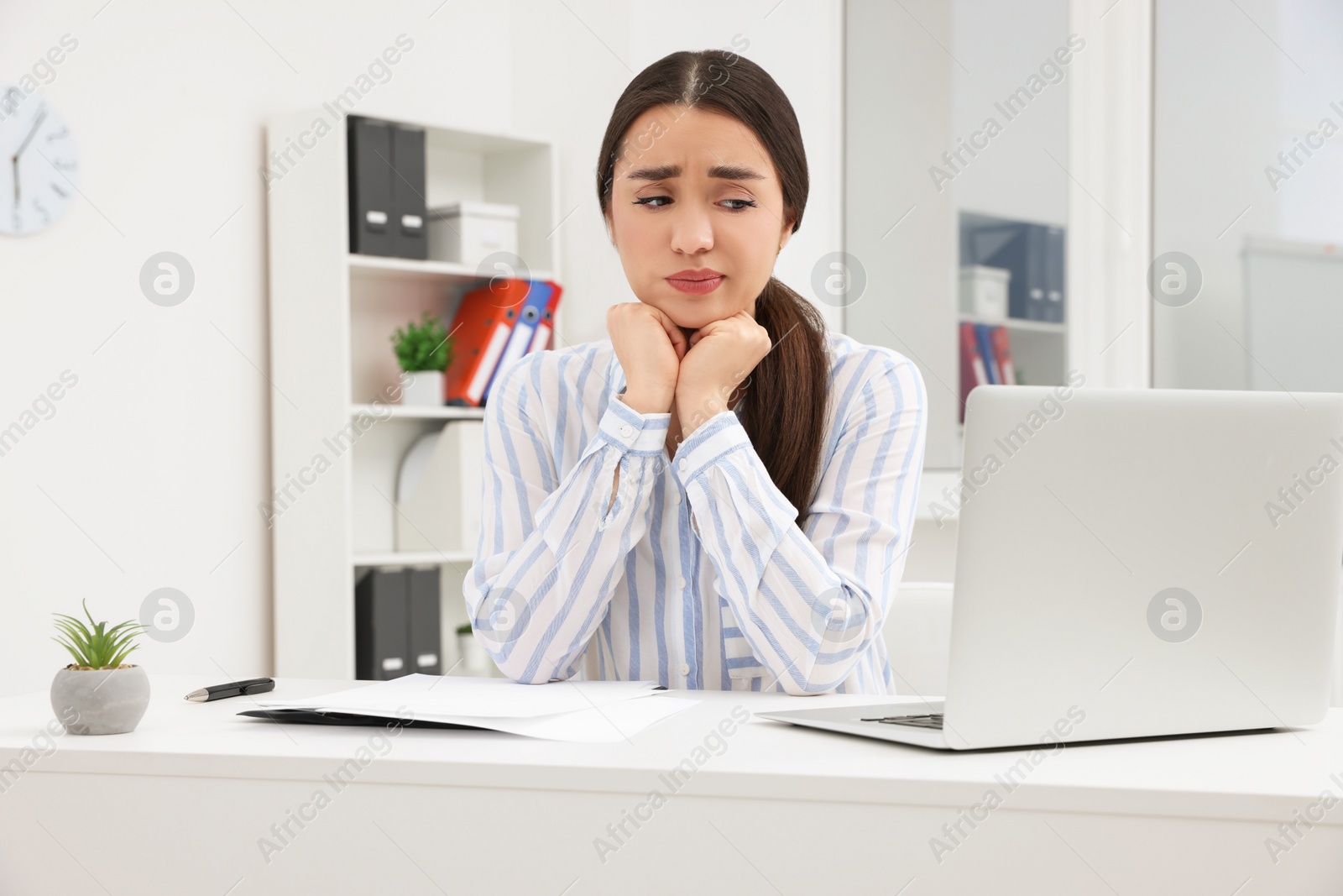 Photo of Unhappy young female intern at table in office