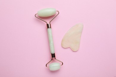 Photo of Gua sha stone and face roller on pink background, flat lay