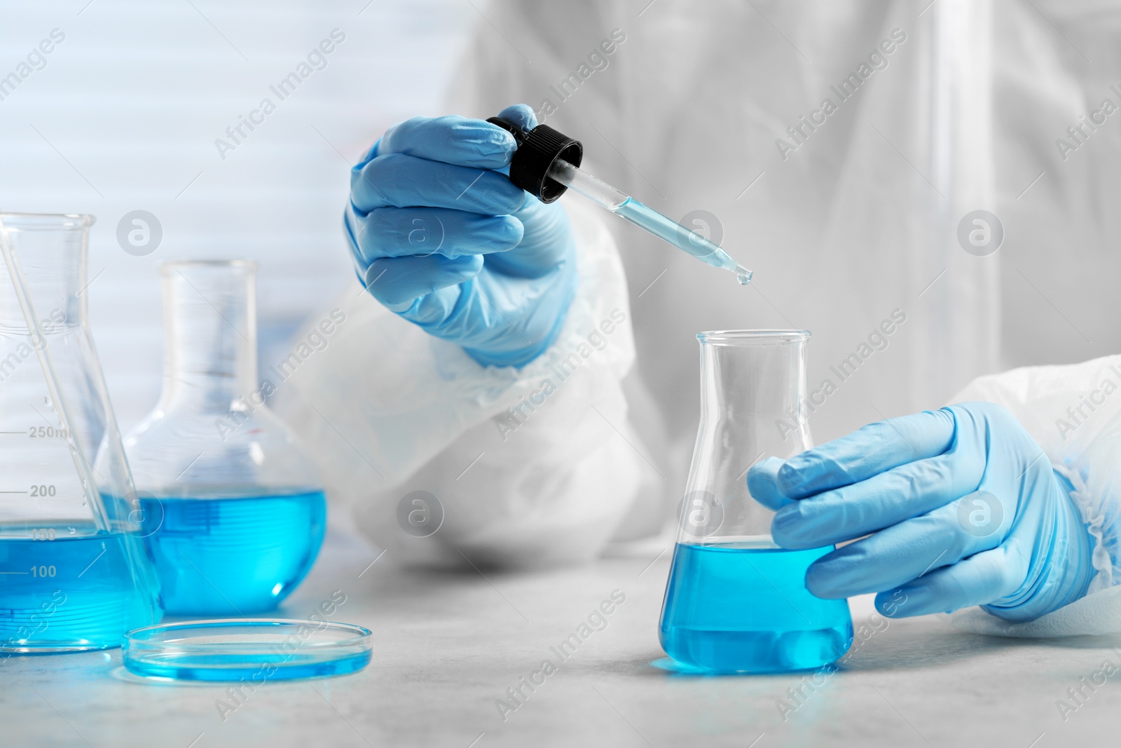 Photo of Scientist dripping liquid from pipette into beaker at white table in laboratory, closeup