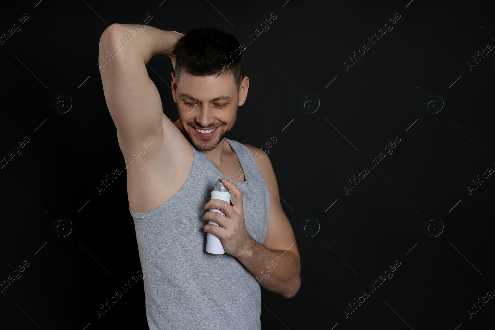 Photo of Handsome man applying deodorant on black background. Space for text