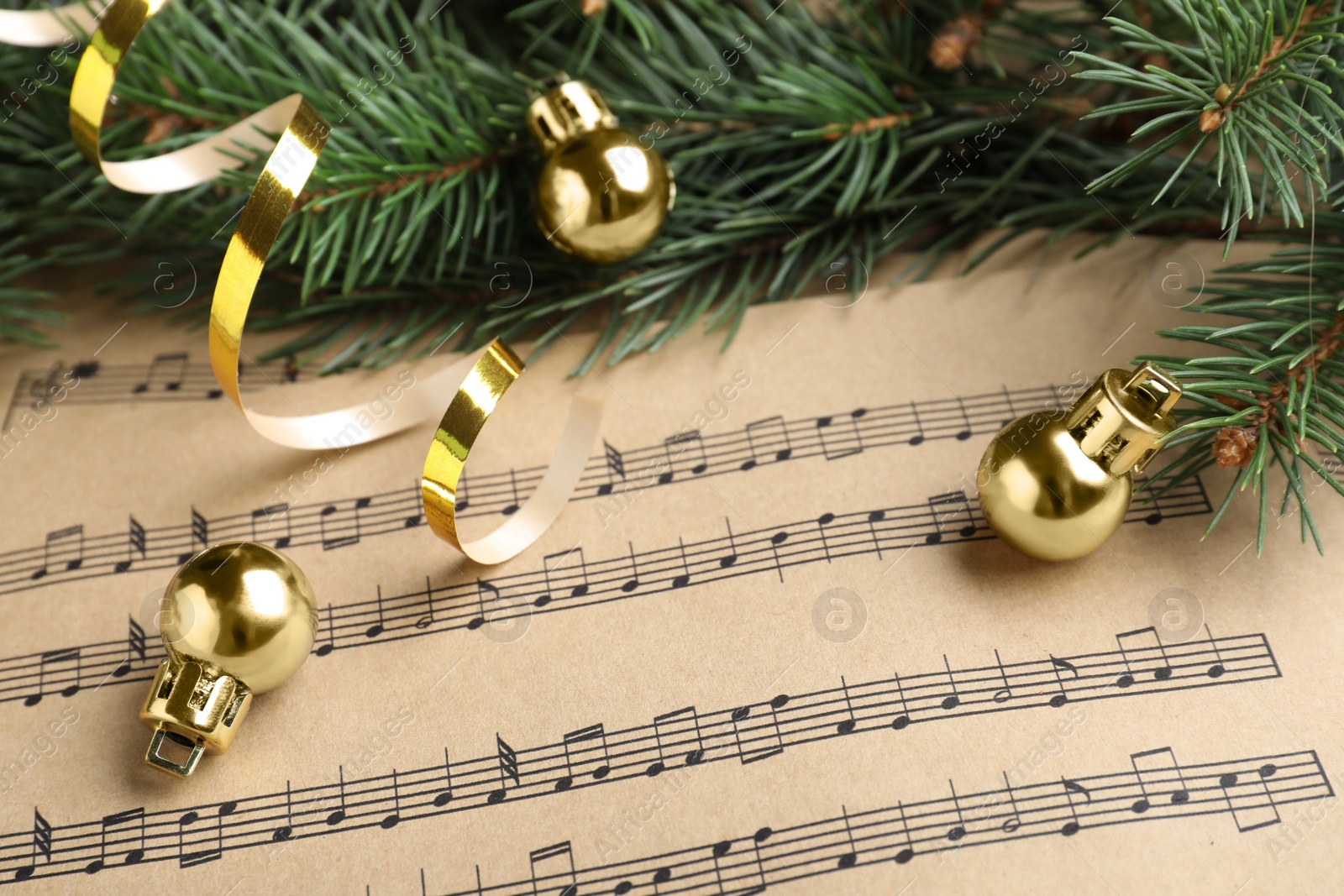 Photo of Fir branches, golden streamer and balls on Christmas music sheets, closeup