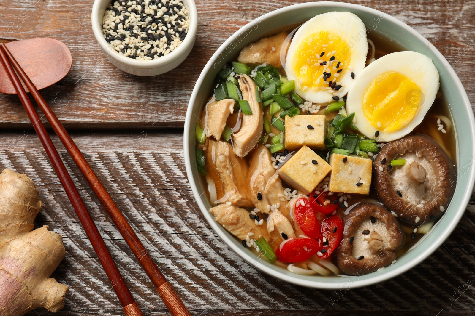 Photo of Bowl of delicious ramen and chopsticks on wooden table, flat lay. Noodle soup