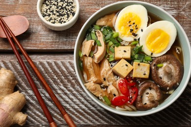 Bowl of delicious ramen and chopsticks on wooden table, flat lay. Noodle soup