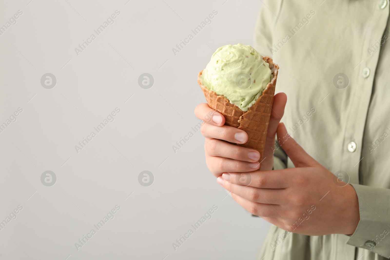 Photo of Woman holding green ice cream in wafer cone on light background, closeup