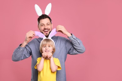 Photo of Father and son in bunny ears headbands having fun on pink background, space for text. Easter celebration
