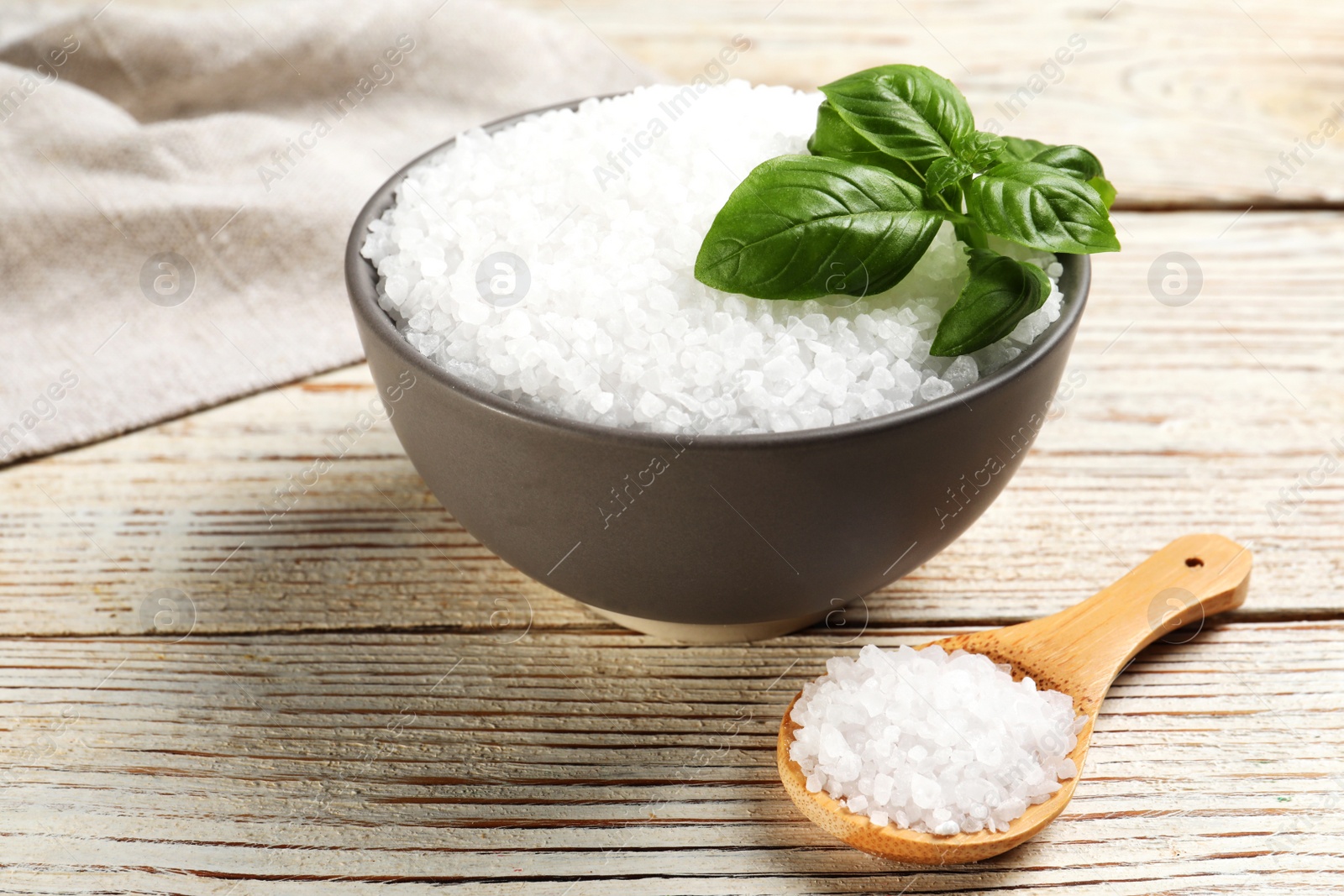 Photo of Bowl and spoon with natural sea salt on white wooden table, closeup