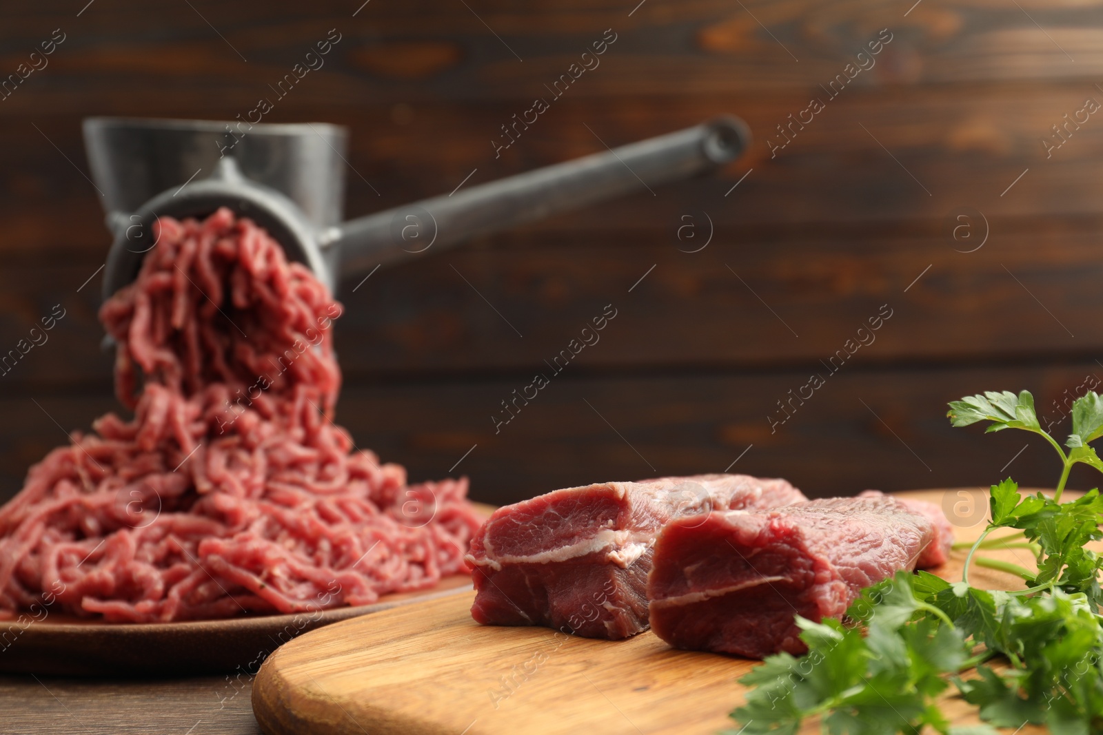 Photo of Manual meat grinder with beef and parsley on wooden table