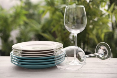 Set of clean dishware and wineglasses on white table against blurred background