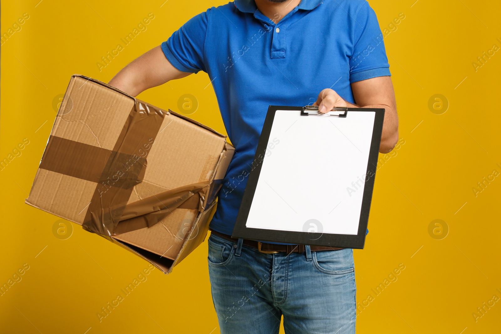 Photo of Courier with damaged cardboard box and clipboard on yellow background, closeup. Poor quality delivery service
