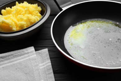Frying pan and bowl with Ghee butter on dark wooden table, closeup
