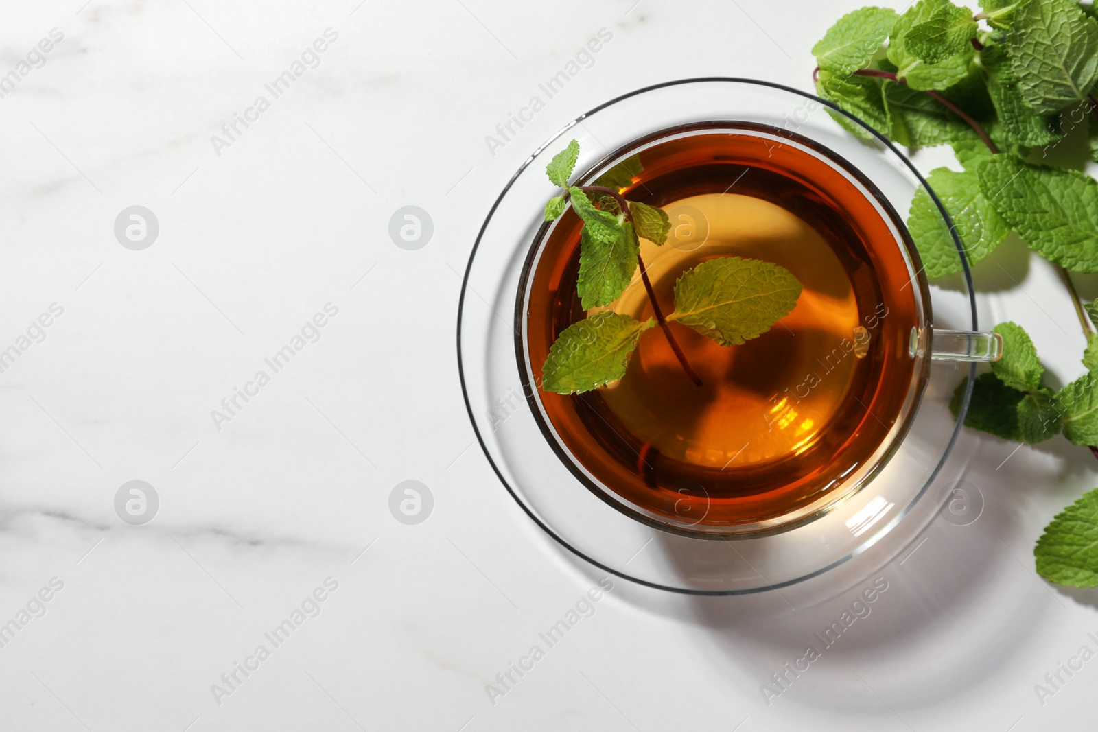 Photo of Cup of aromatic herbal tea with mint on white marble table, flat lay. Space for text