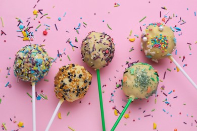 Photo of Delicious confectionery. Sweet cake pops and sprinkles on pale pink background, flat lay