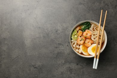 Delicious ramen with shrimps and chopsticks on grey table, top view with space for text. Noodle soup