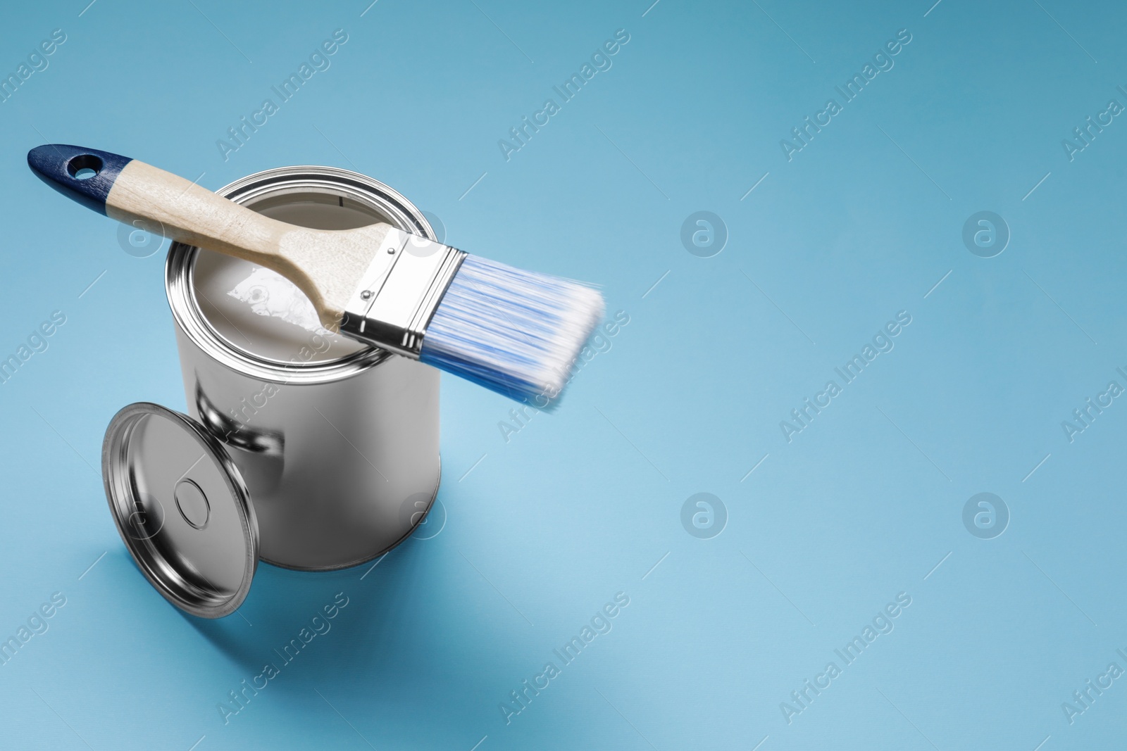 Photo of Can with white paint and brush on light blue background, space for text
