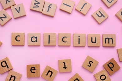 Word Calcium made of wooden cubes with letters on pale pink background, top view