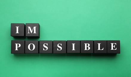 Motivation concept. Changing word from Impossible into Possible by removing black wooden cubes on green background, flat lay