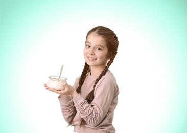 Cute girl eating tasty yogurt on color background