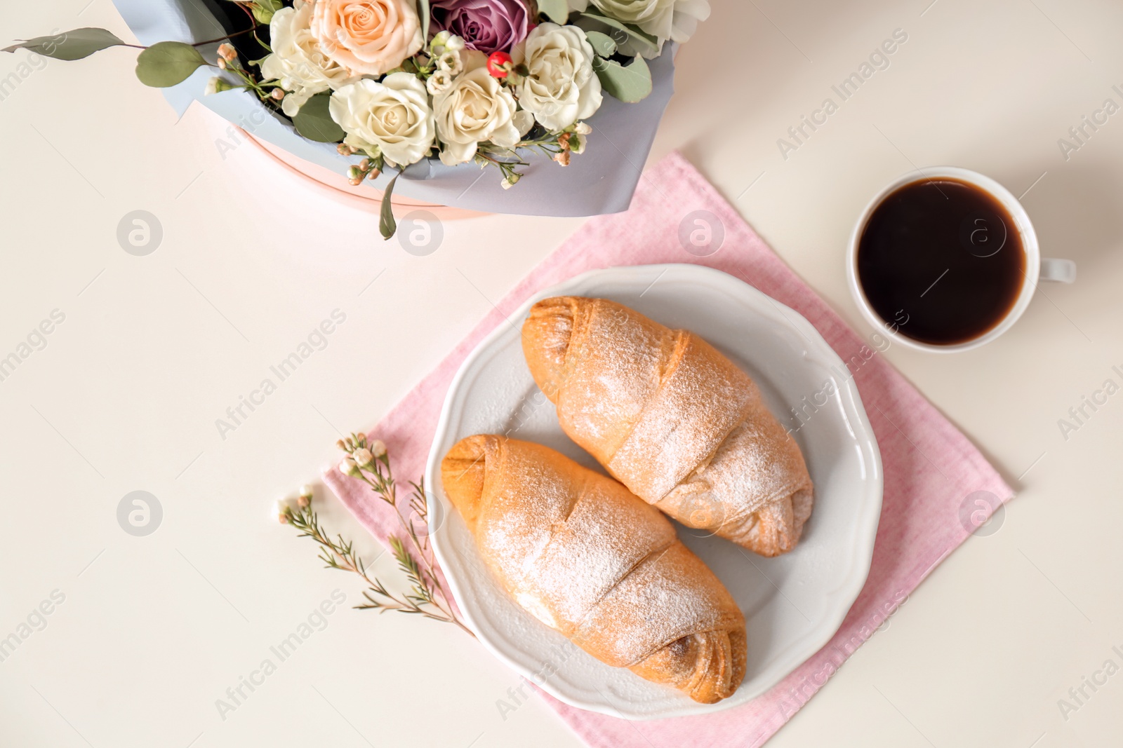 Photo of Plate with delicious croissants, cup of coffee and flowers on light background, top view